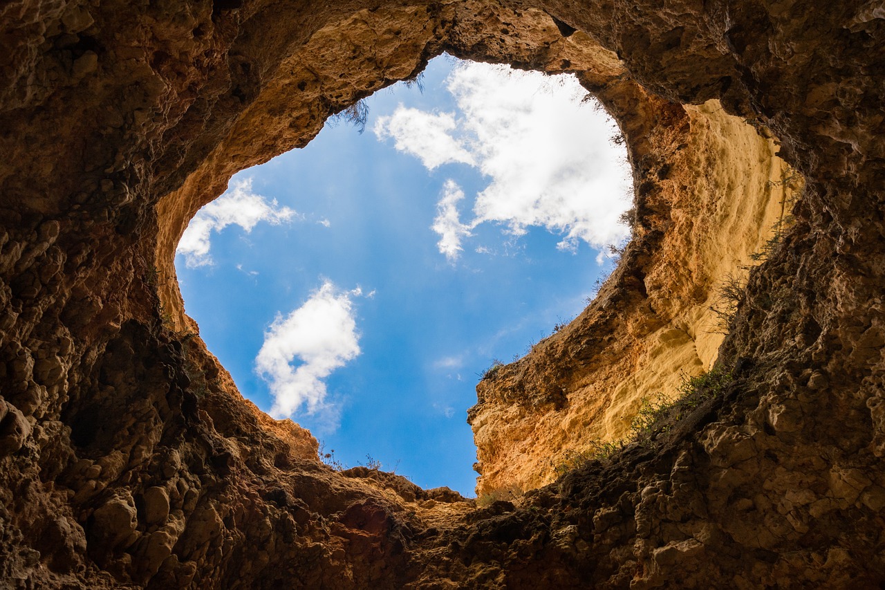 Looking out of a deep hole in the earth up into a blue sky.