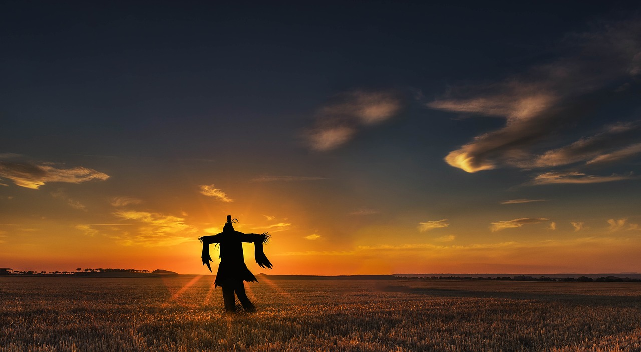 A silhouette of a scarecrow in a flat field backed by dramatic sun rays.